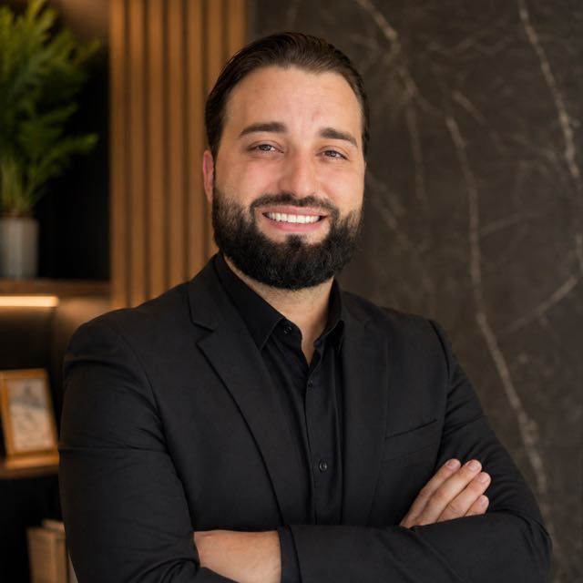 Dr. Bruno Portal, cirurgião-dentista, de terno escuro e braços cruzados no consultório